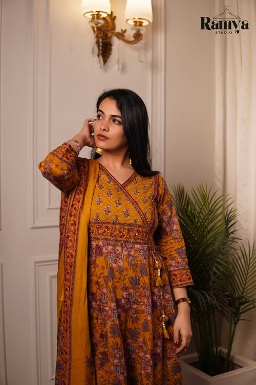 Woman in a mustard yellow and purple patterned outfit standing indoors with decorative elements.