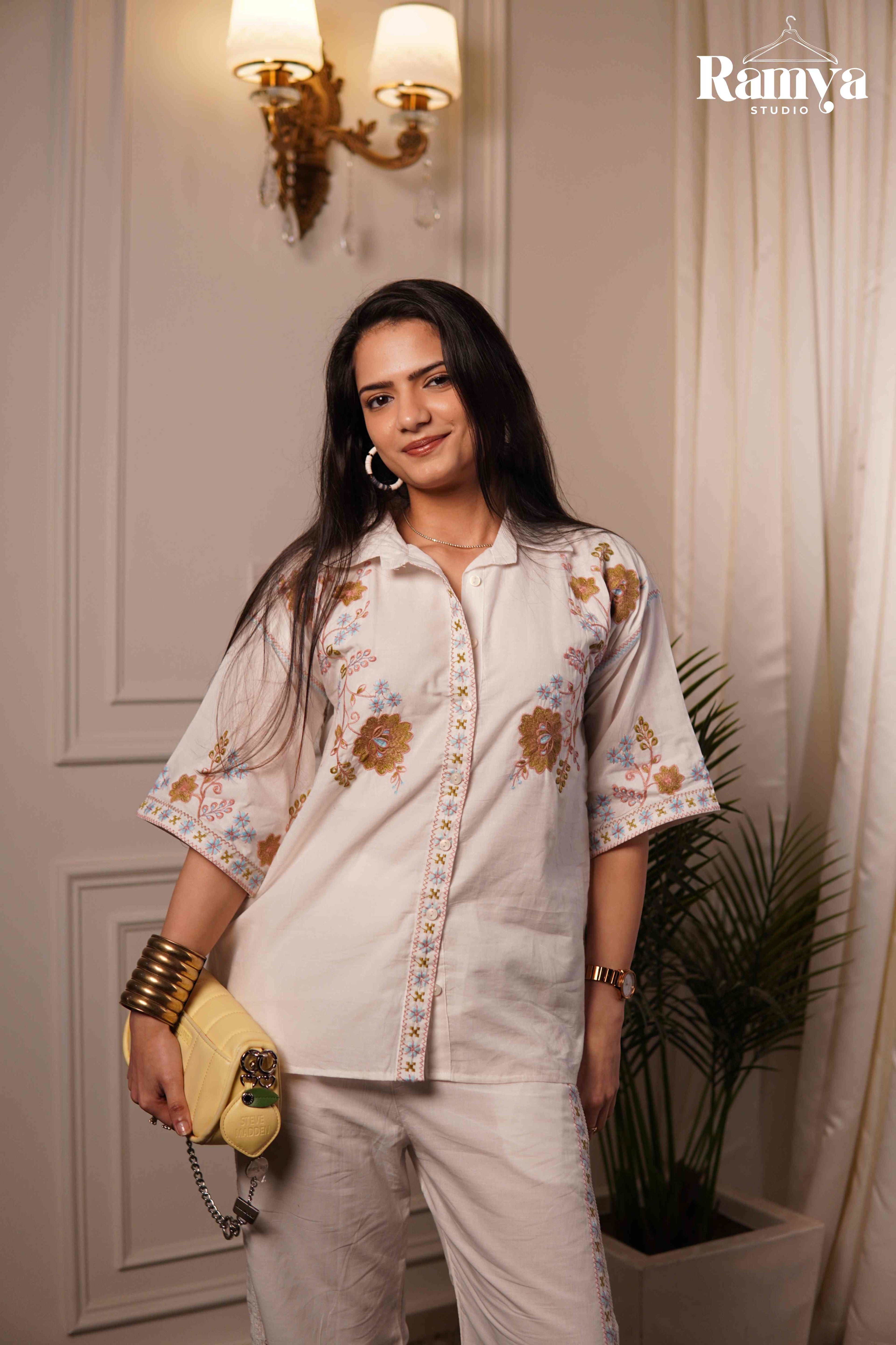 Woman wearing a white embroidered shirt and pants, holding a yellow clutch, standing indoors.
Ivory Bloom co-ord set for women elegant off-white matching top and bottom set, handpicked limited edition ethnic wear by Ramya Studio
