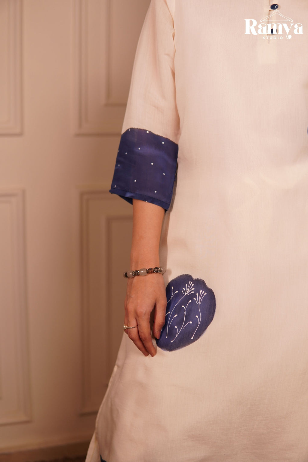 Close-up of the delicate white thread work embroidery inside an indigo applique patch on a cream tunic, highlighting matching fabric buttons and a fine dot print.