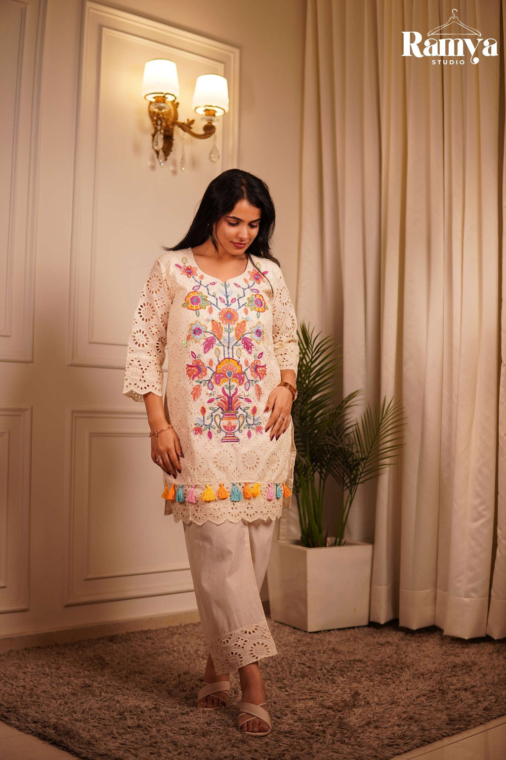 Boho-chic Indian resort wear: A model styling an ivory embroidered tunic set with cream cross-strap sandals against a luxurious minimalist home backdrop.