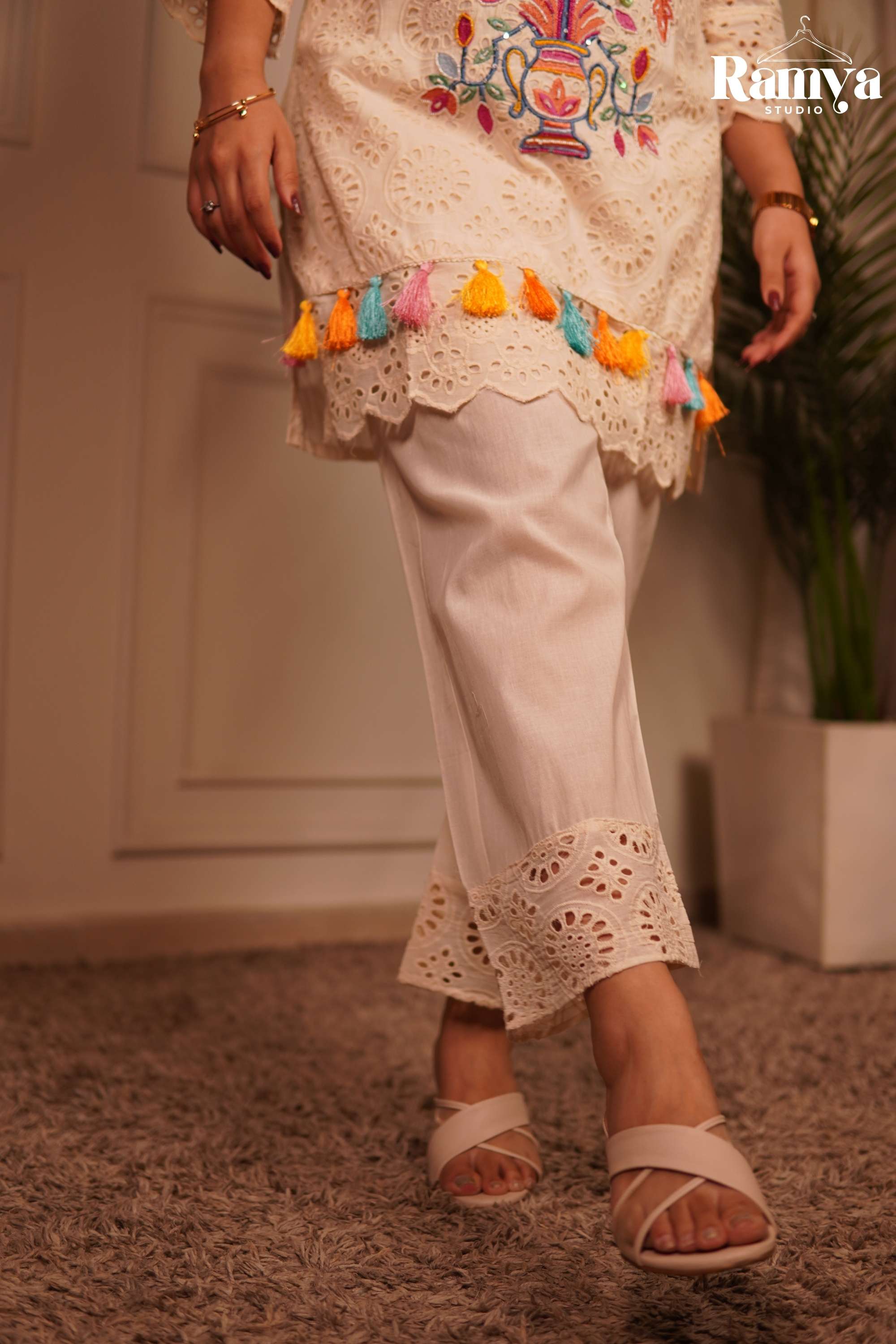 Close-up of a white eyelet lace short kurta with scalloped hems, colorful fringe thread tassels, and traditional botanical thread work on the yoke.
