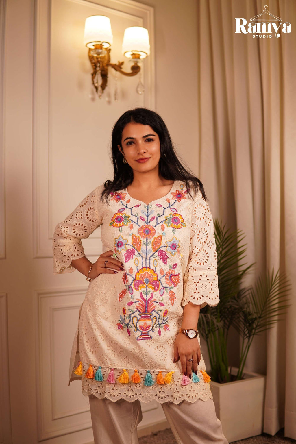 Boho-chic Indian resort wear: A model styling an ivory embroidered tunic set with cream cross-strap sandals against a luxurious minimalist home backdrop.