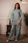 A model standing in the Ramya Exclusive 'Pistachio Poppy' 2-piece set, highlighting lilac floral embroidery, dark ladder-lace side trims, and white woven sandals