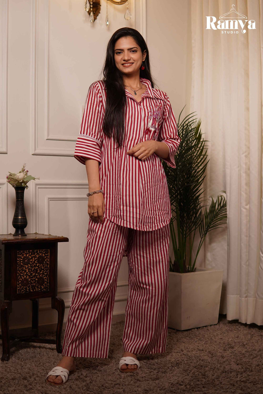 A model standing in a relaxed-fit red and off-white striped tunic set, highlighting wide-leg trousers and a resort-style collar.