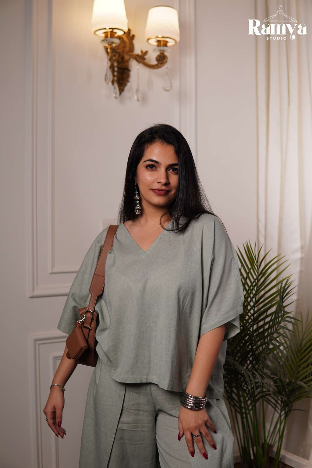 A minimal sage green loungewear set for women featuring a lightweight, textured fabric, relaxed V-neck tunic top, and high-waisted wrap-style trousers with fluid drape movement.