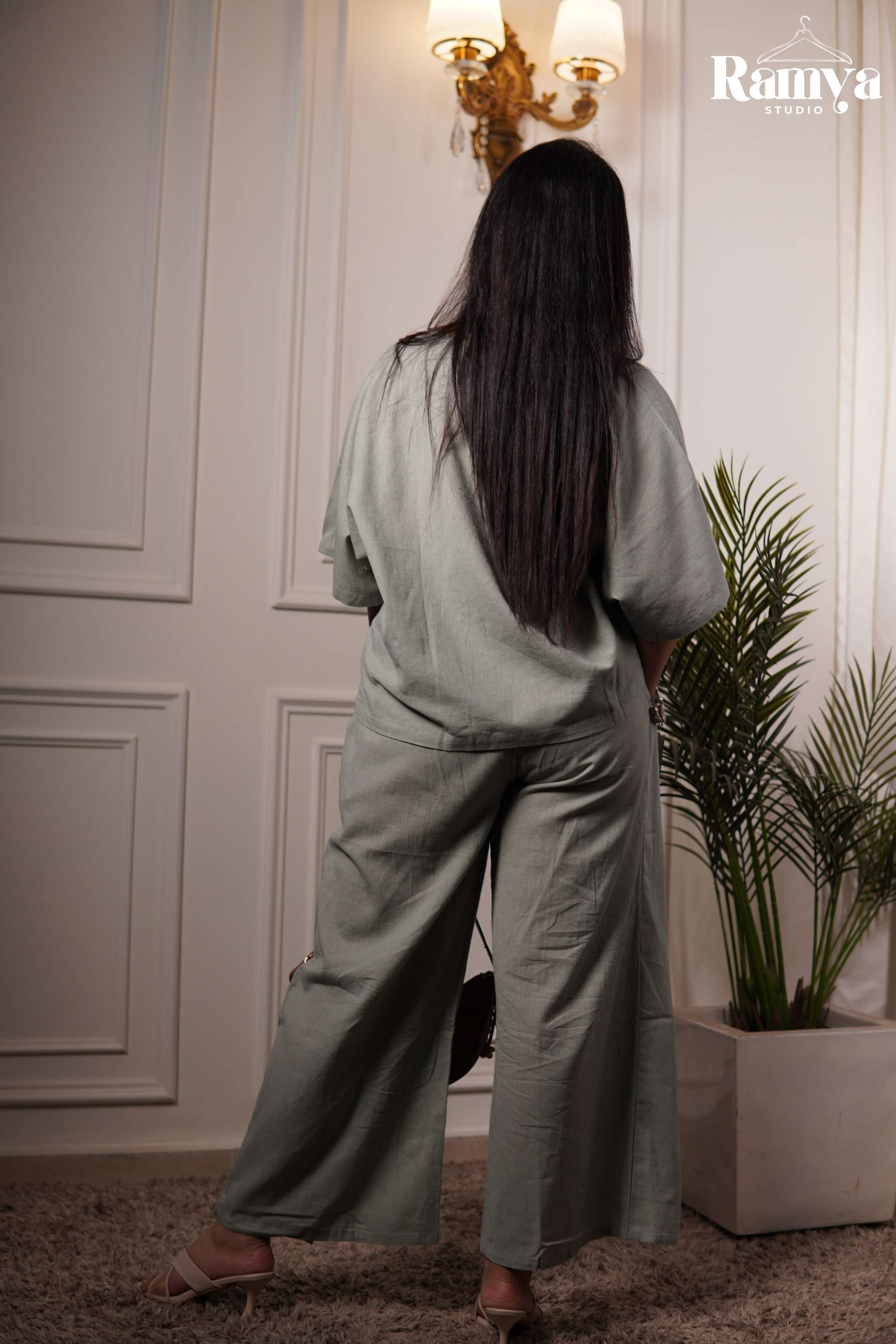 A minimal sage green loungewear set for women featuring a lightweight, textured fabric, relaxed V-neck tunic top, and high-waisted wrap-style trousers with fluid drape movement.