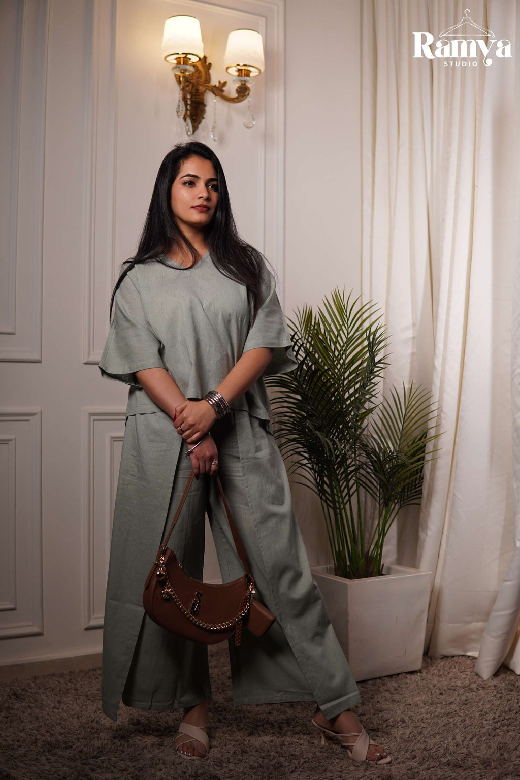 A model posing in Ramya Studio's sage green essential co-ord set, featuring a relaxed-fit, boxy short-sleeve top with a V-neckline and matching wide-leg trousers with front overlay panels.