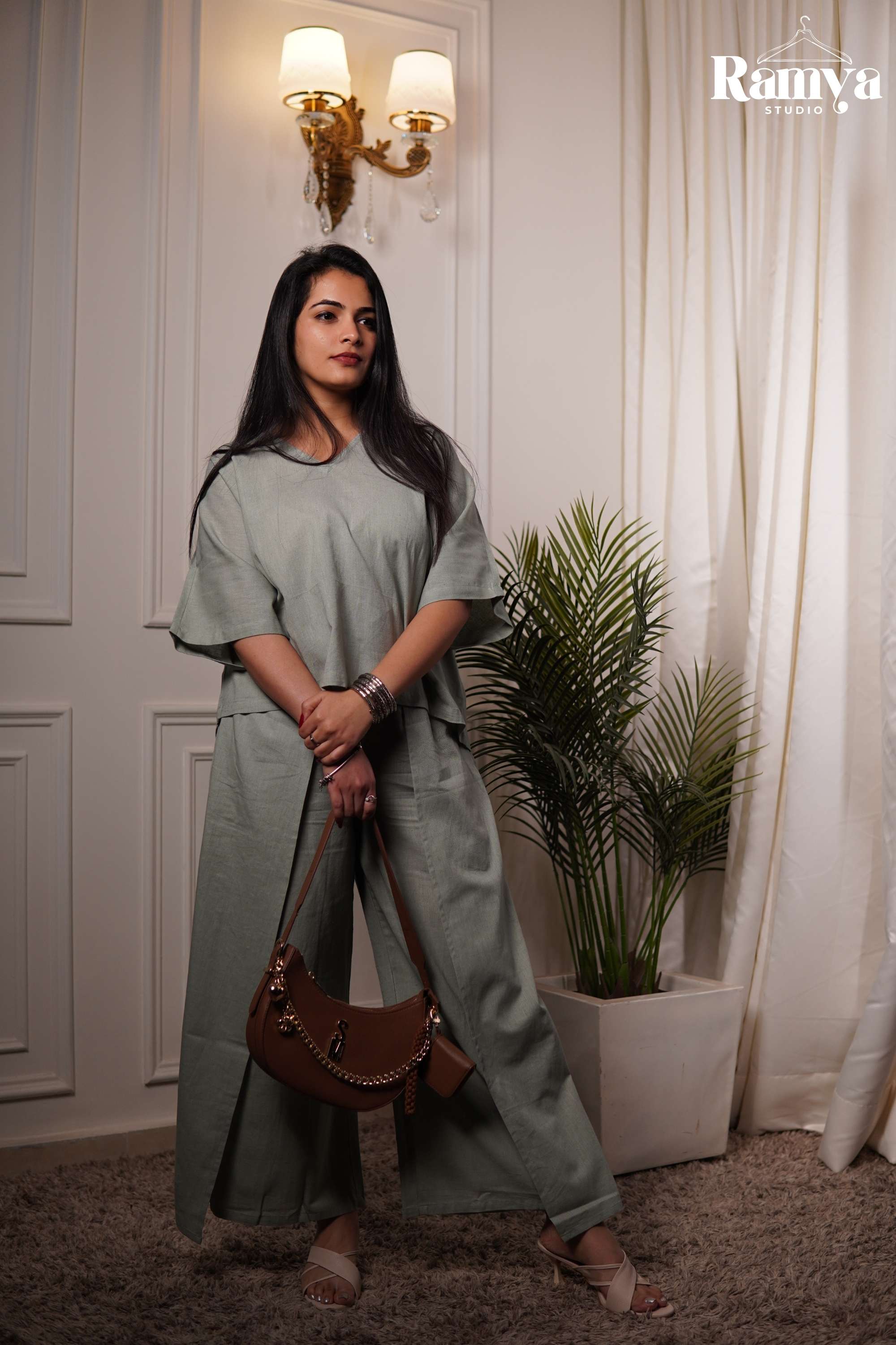 A model posing in Ramya Studio's sage green essential co-ord set, featuring a relaxed-fit, boxy short-sleeve top with a V-neckline and matching wide-leg trousers with front overlay panels.