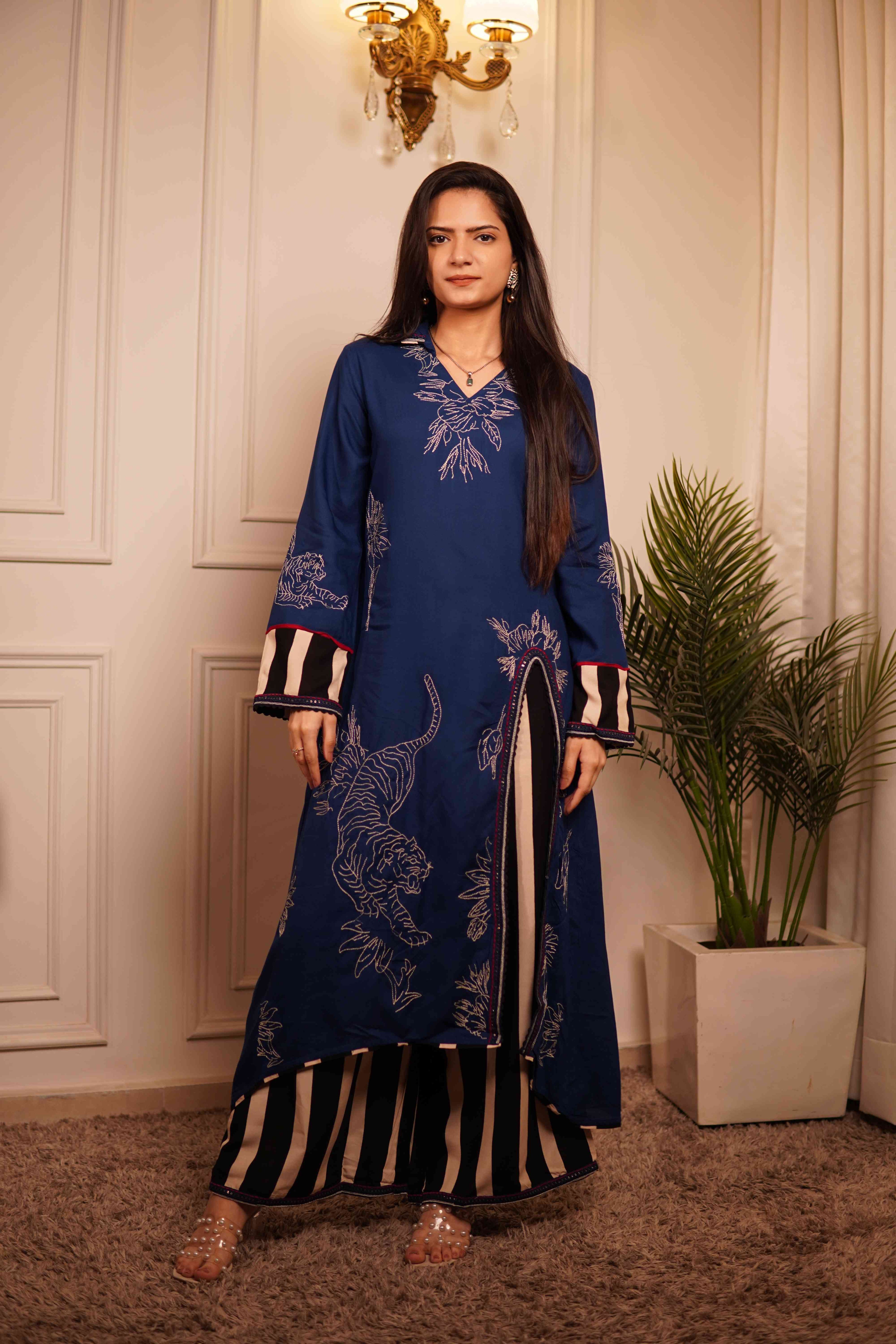Modern Indian fusion wear: Deep blue tunic with animal print motifs paired with bold vertical striped culottes, styled with transparent block heels in a luxury interior setting.