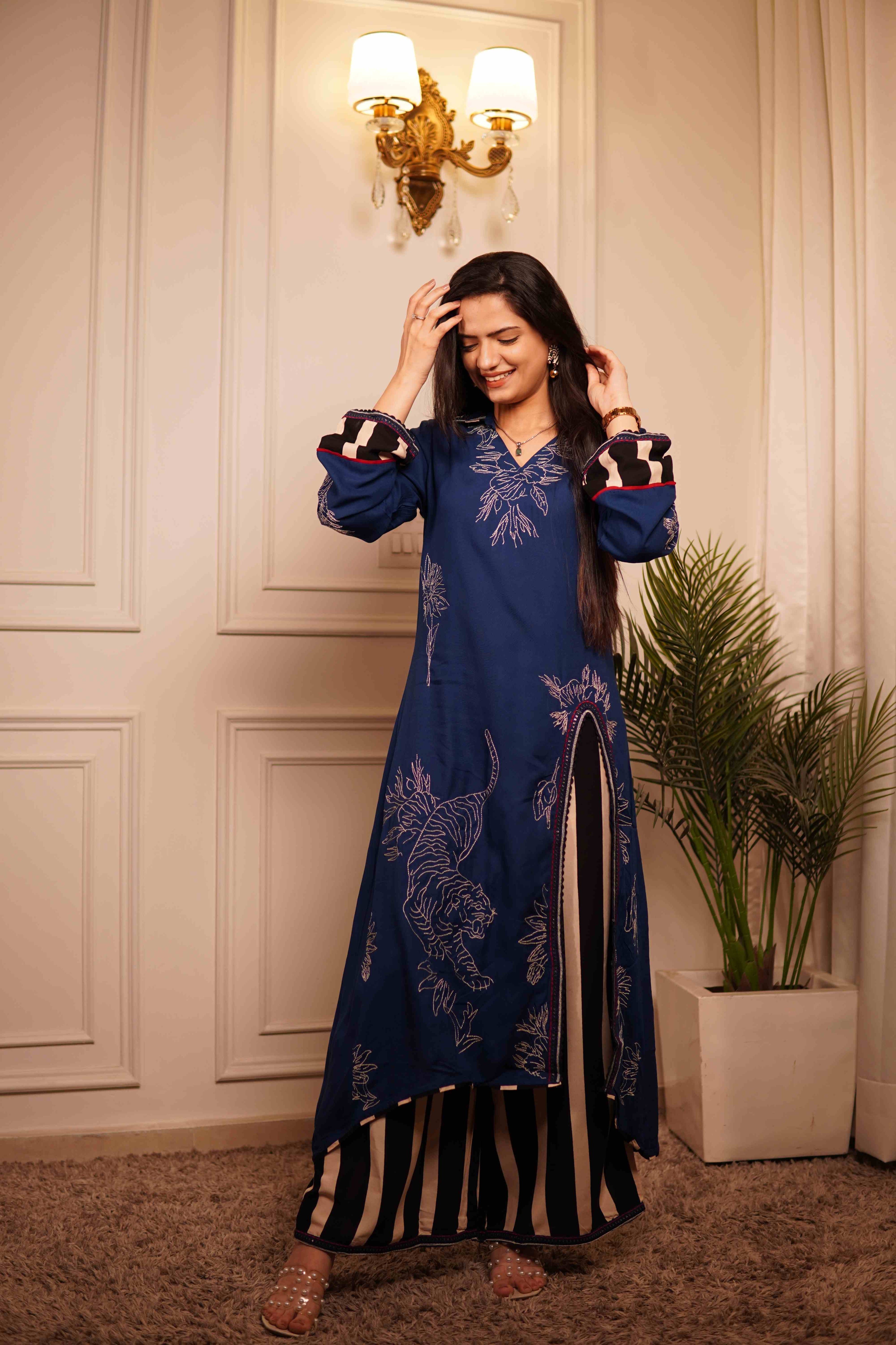 Full-length view of a women's ethnic co-ord set in dark blue fabric with white tiger and floral line-art embroidery, featuring long sleeves with striped cuffs and striped flared trousers.