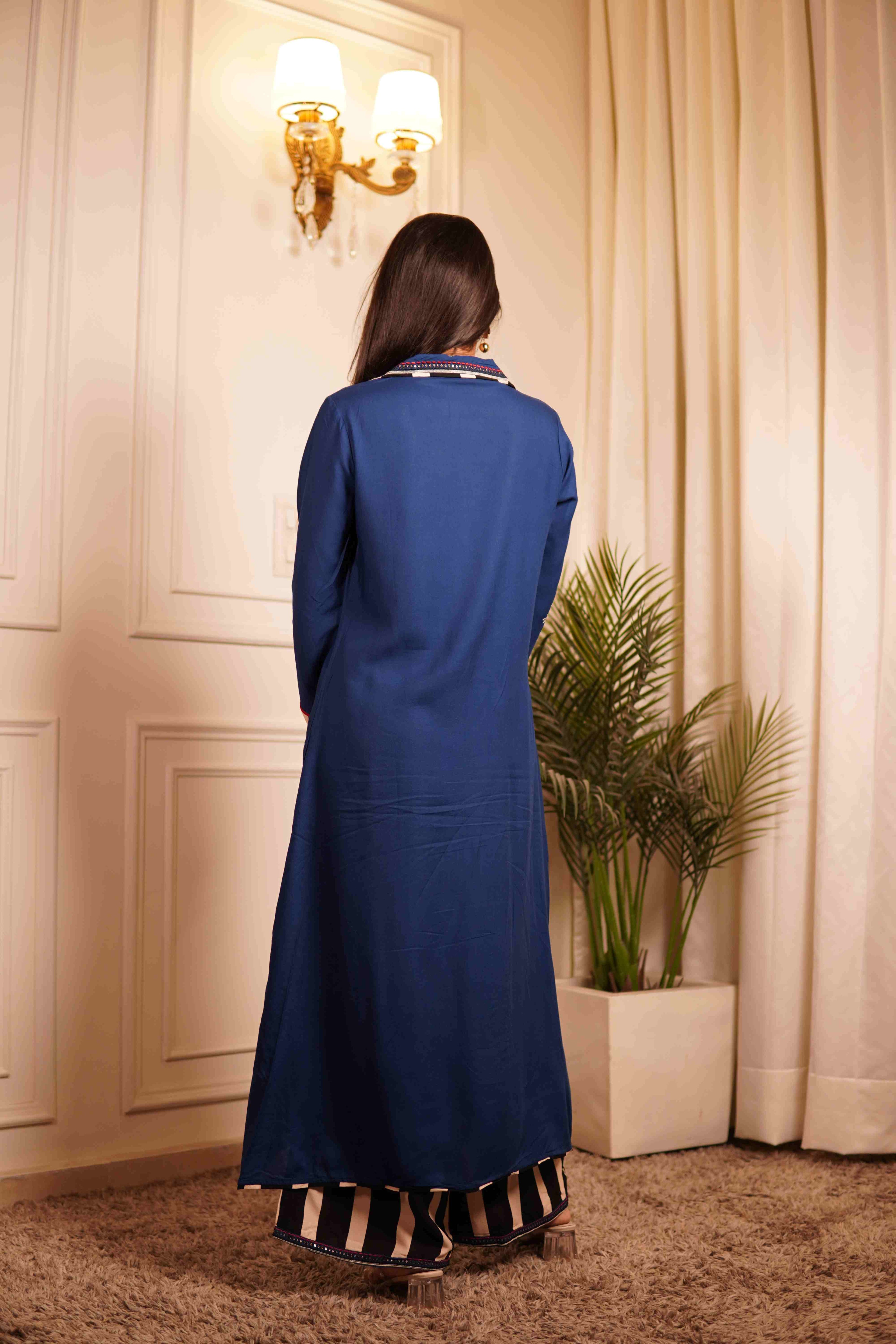 Woman wearing a blue co-ord set standing in a room with white walls and a plant.