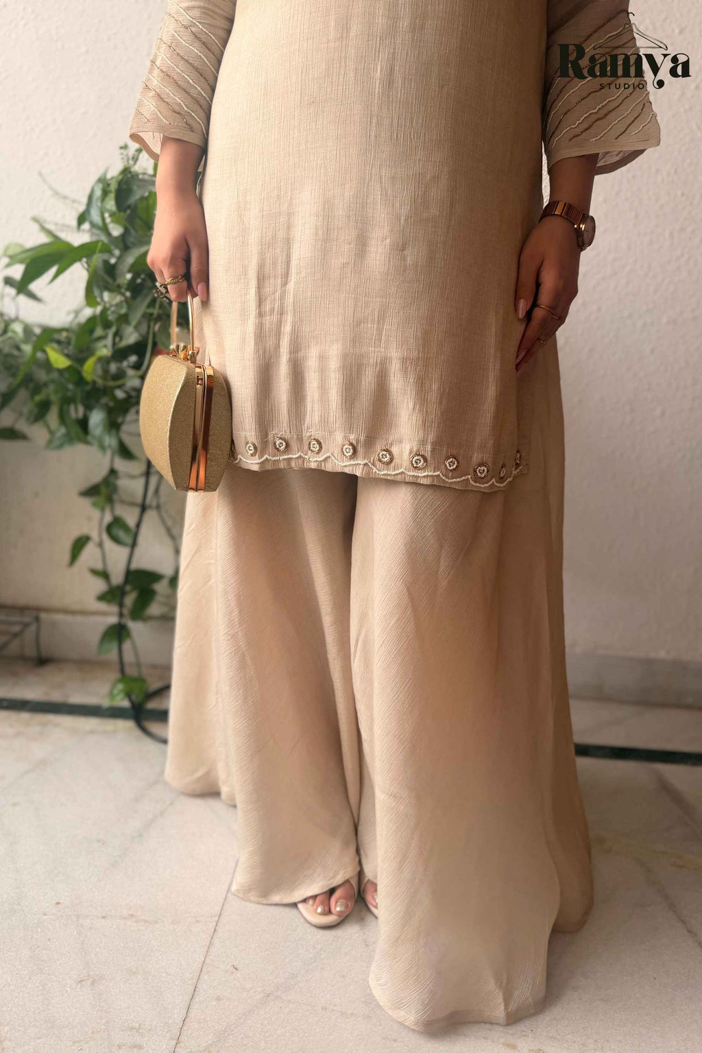 A model wearing Ramya Studio's Geet Ivory Sharara Set holding a gold clutch.
You can see the embroidery detailing and the zoomed in look of the sharara