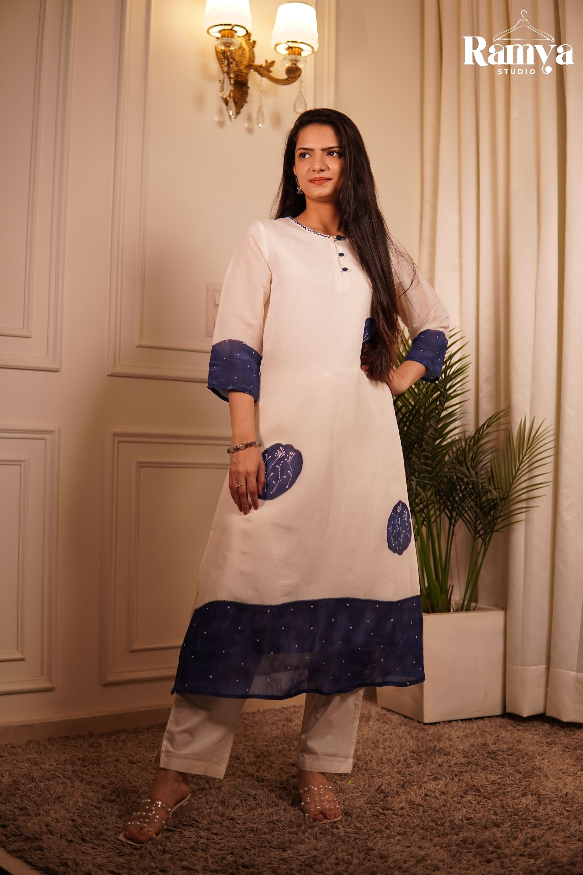 A model posing in Ramya Studio's 'The Indigo Flora Edit', featuring a premium ivory kurta set with deep indigo-blue circular patches and hand-embroidered white flower stems