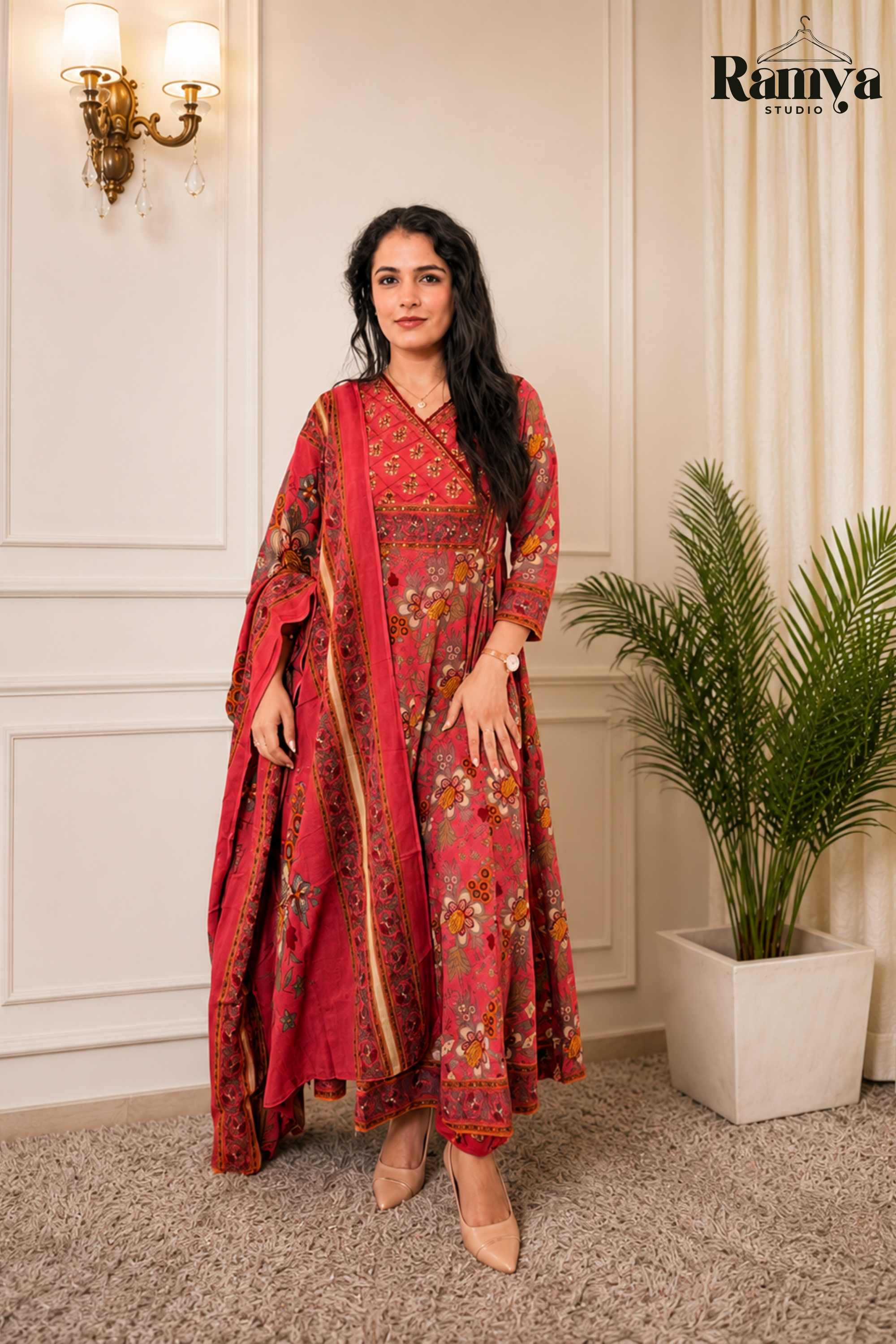 A model wearing Ramya Studio's 'The Raani Anarkali', a crimson red printed Angrakha suit set with a sweeping flare, matching printed dupatta, and nude pumps.