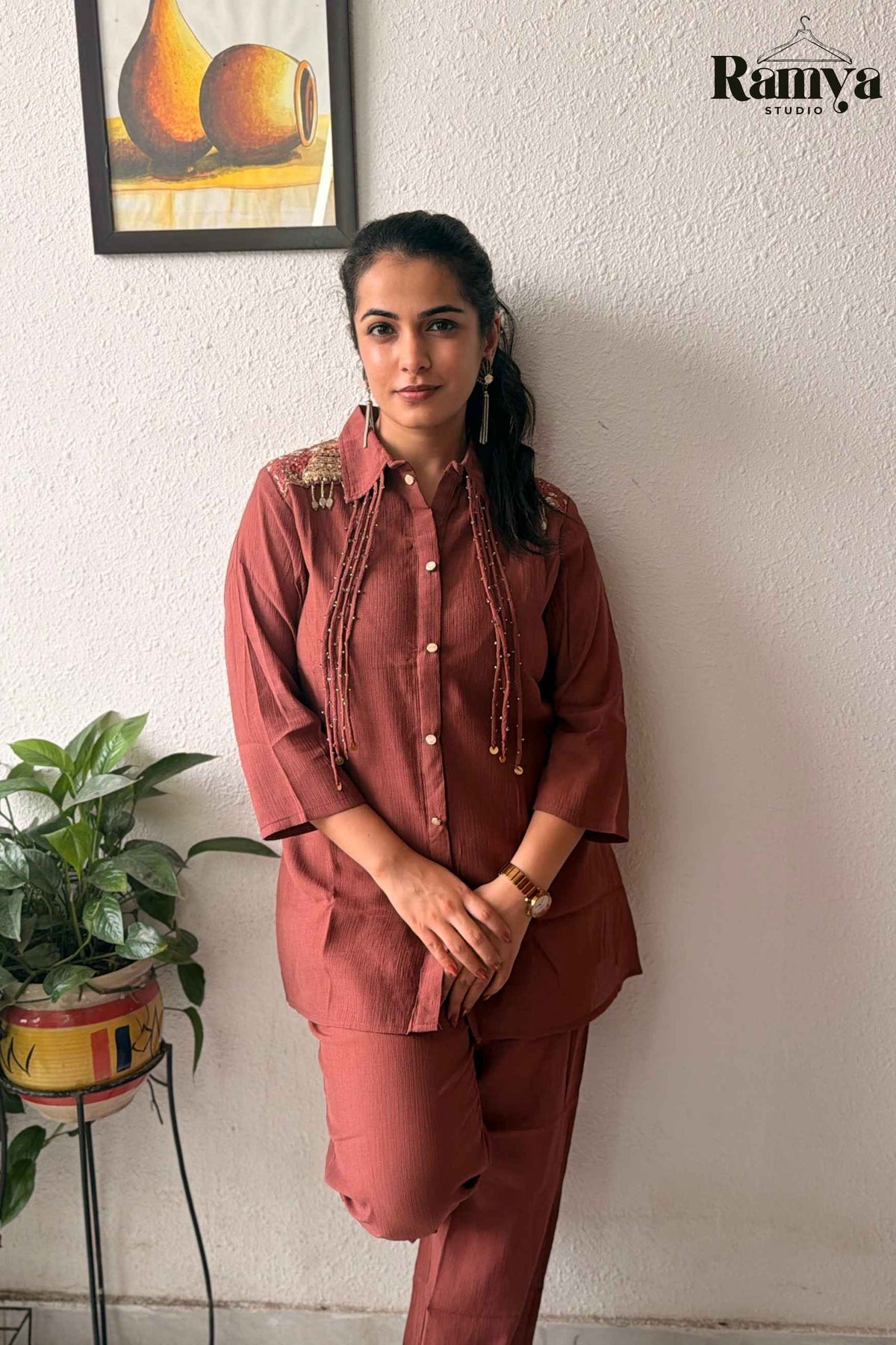Frontal pose of a model wearing Ramya Studio's 'Rumi' set in terracotta rust with shoulder embroidery and beaded coin strands