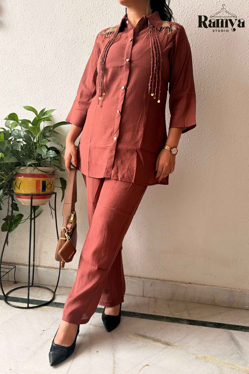 Three-quarter pose of a woman wearing the 'Rumi' terracotta co-ord set with long drop earrings and classic watch.