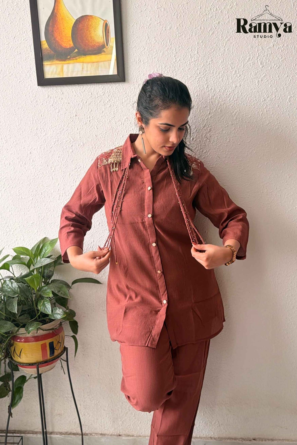 Model leaning against a wall in the 'Rumi' rust-colored tunic set showcasing the cascading beaded detailing.