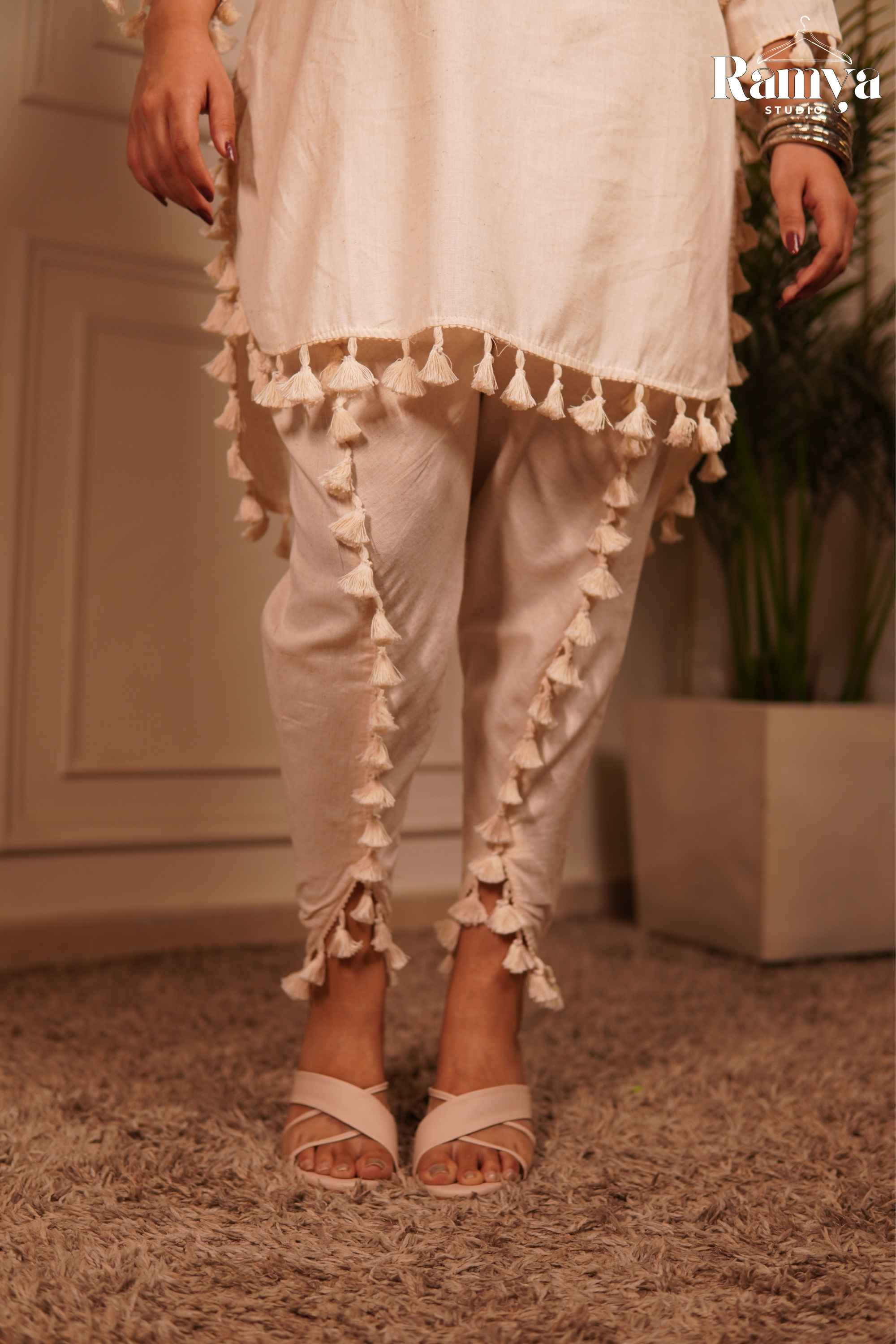 Detailed shot of the overlapping tulip-slit trousers featuring continuous white tassel trim along the leg seam and hem.