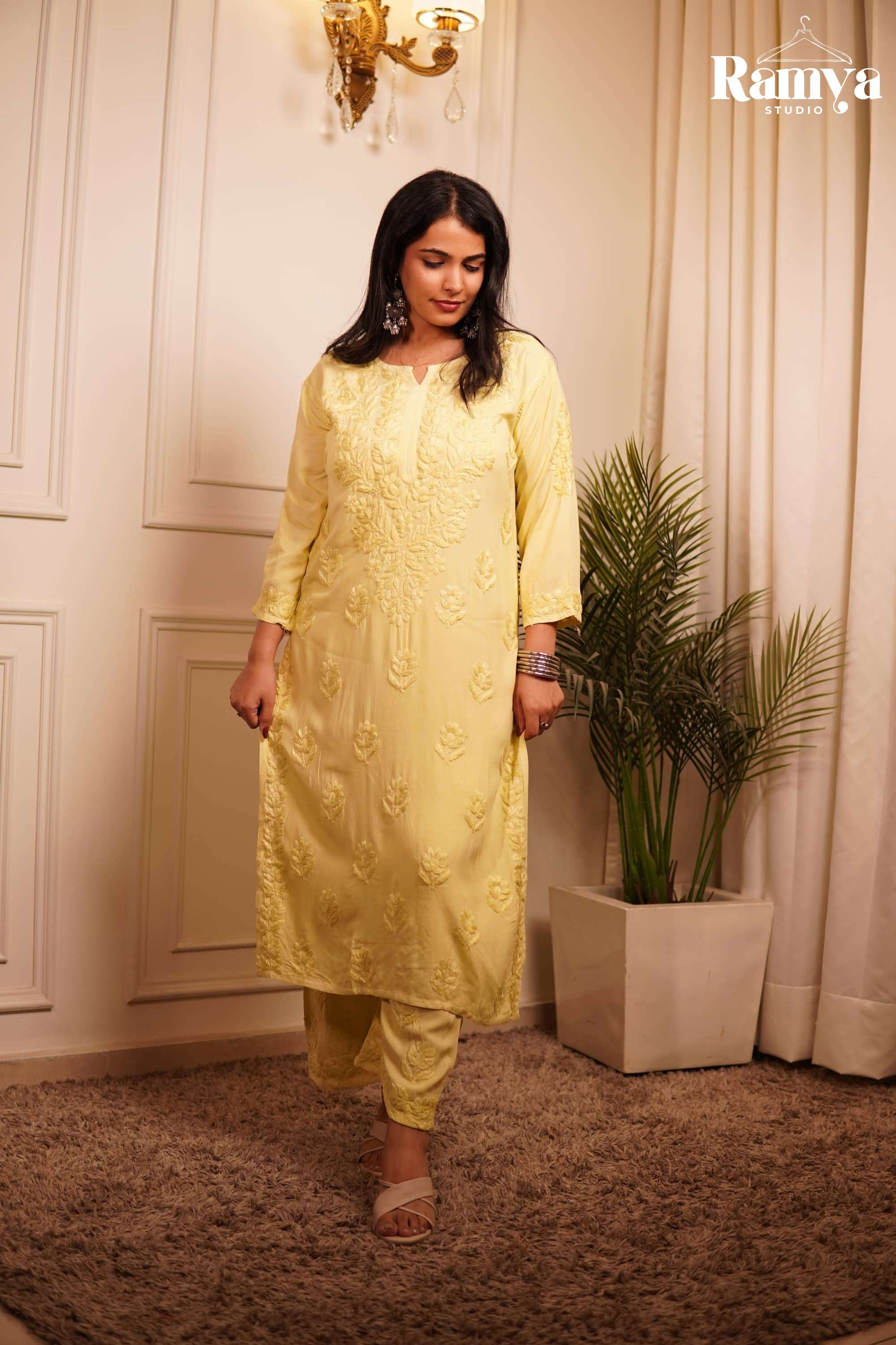 Chic summer ethnic fashion: A model wearing an ultra-breathable pastel yellow embroidered tunic and pant set, styled with nude cross-strap flats in a premium, warm-lit home interior setting.
