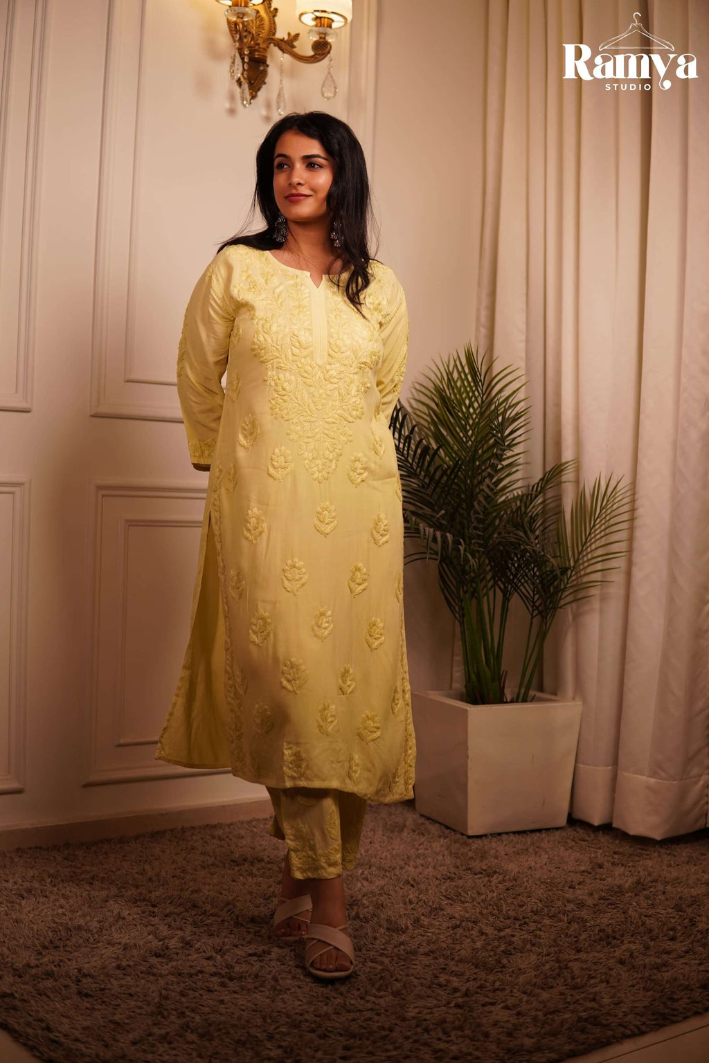 Full-length view of a women's 2-piece cotton-rayon ethnic suit in light yellow, decorated with all-over traditional tonal Chikankari thread embroidery, a split V-neckline, and comfort-fit matching trousers.
